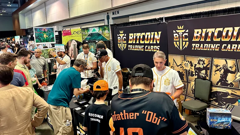 A crowd of attendees gathered at the Bitcoin Trading Cards booth beneath its banner