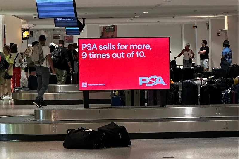 A large red PSA advertising screen in an airport baggage hall reading “PSA sells for more, 9 times out of 10”