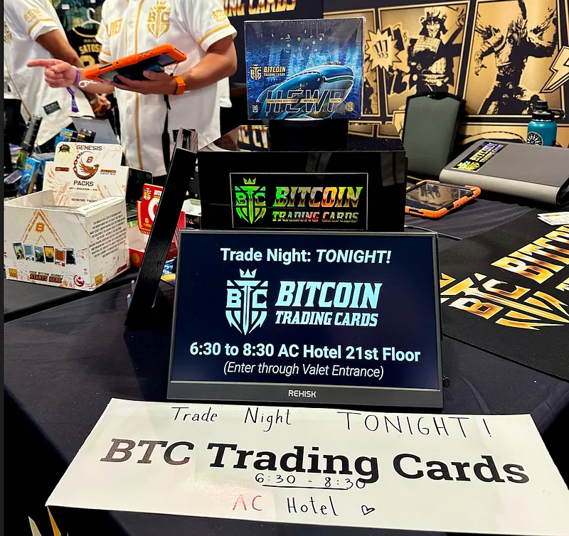 A sign on the Bitcoin Trading Cards booth reading “Trade Night: TONIGHT! 6:30 to 8:30 AC Hotel 21st Floor”, beside a handwritten sign for the same event