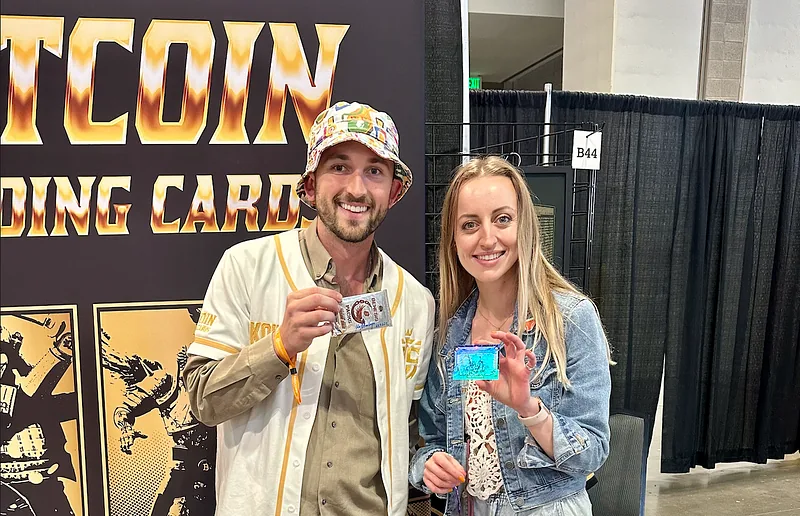 Artist Flo Montoya and Koil standing at the Bitcoin Trading Cards booth, each holding a signed card