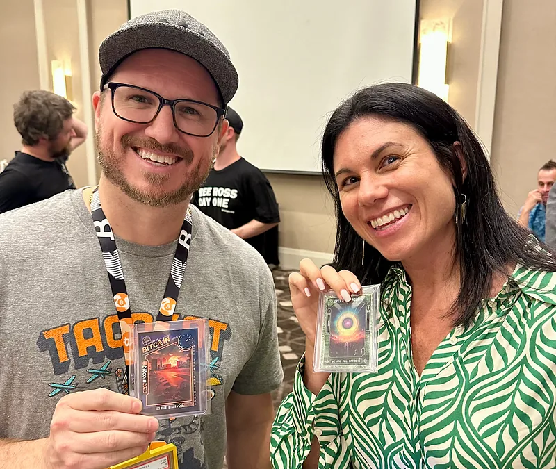 Two collectors smiling at the conference, each holding a numbered Bitcoin Trading Card they have just traded for