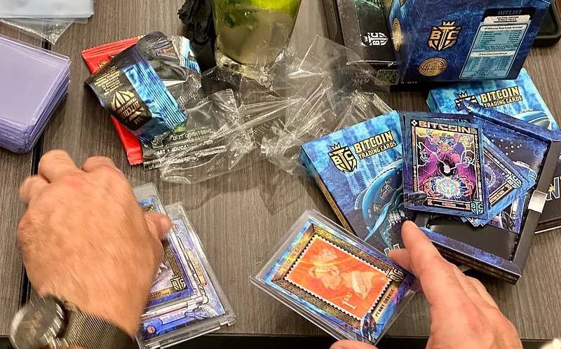 Hands sorting through opened Bitcoin Trading Cards packs and sleeves spread across a table